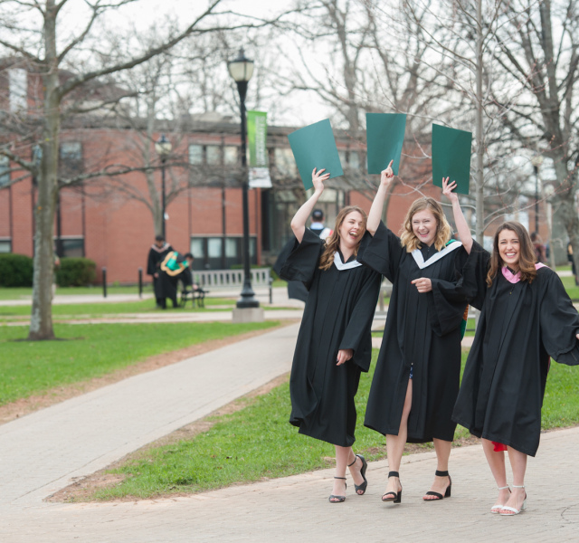 three BCA graduates holding degrees in the quadrangle